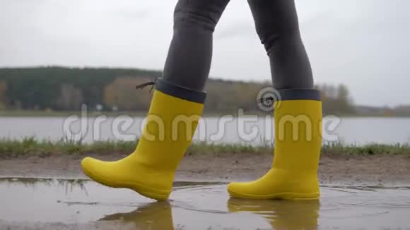 黄靴女子的腿在阴云的秋日穿过水坑视频的预览图