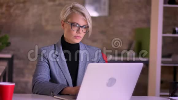 金发短发的女商人戴着眼镜在办公室里用笔记本电脑做按摩视频的预览图