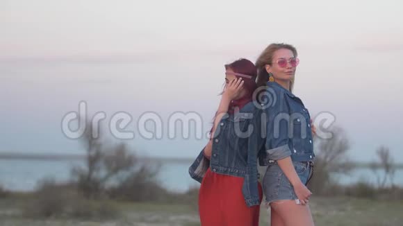 两个穿着牛仔夹克的年轻女子背靠背站着头发迎风飘扬视频的预览图