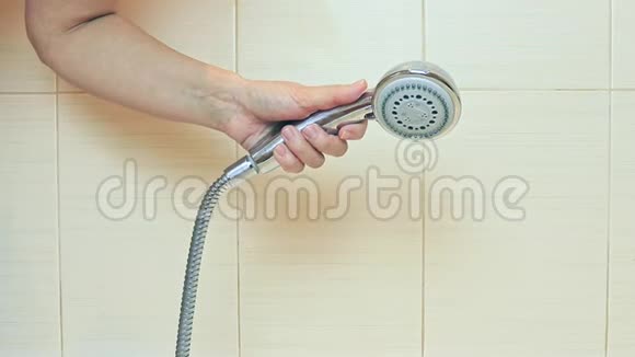 一个女人她的手在浴室里拿着一个淋浴头打开水试着水温并关掉它视频的预览图