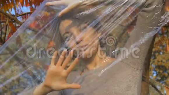 一位金发短发的年轻女子透过塑料袋站在户外的聚乙烯包裹阳光明媚视频的预览图