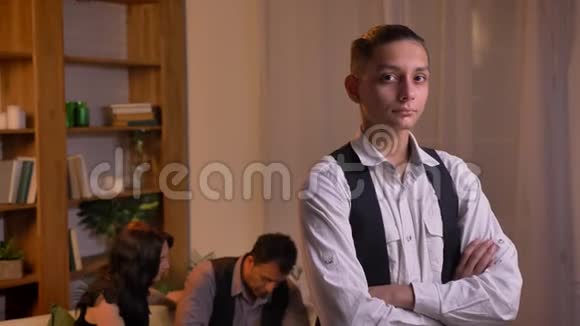 十几岁的阿拉伯男孩的肖像直接观看镜头与手臂交叉和他的家庭背景视频的预览图