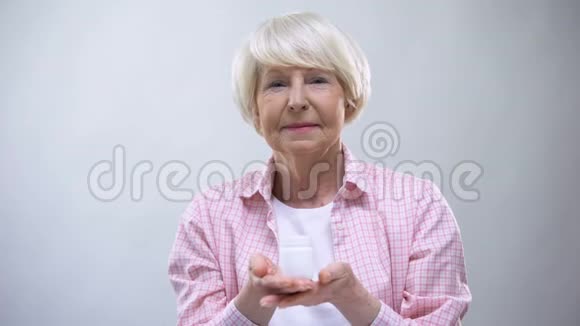 微笑老年女性在镜头中显示补充剂健康支持维生素视频的预览图