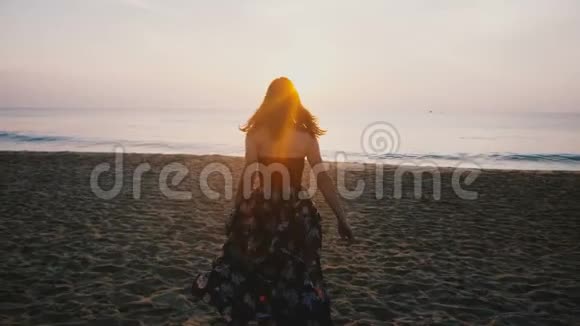 镜头跟随年轻的旅游妇女穿着漂亮的裙子在史诗般的田园诗般的异国情调度假海滩上朝日落跑去视频的预览图