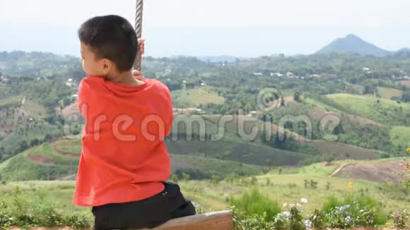 男孩拉着绳子摇着摇椅快乐地玩耍背景山在泰国的KhaoKho风电场里视频的预览图