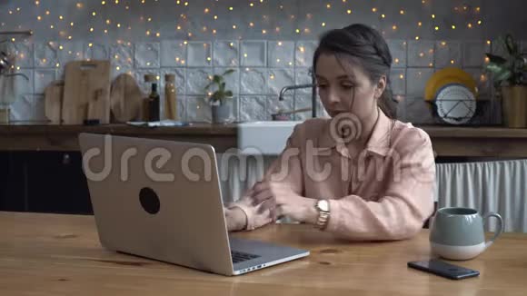 一位年轻貌美的年轻女士坐在厨房里用笔记本电脑工作库存录像现代视频的预览图