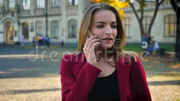 年轻的女学生在大学外面打电话心烦意乱看着手表在外面等待视频的预览图