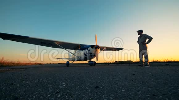 飞行员看着飞机男飞行员站在跑道上看着日落背景下的飞机视频的预览图