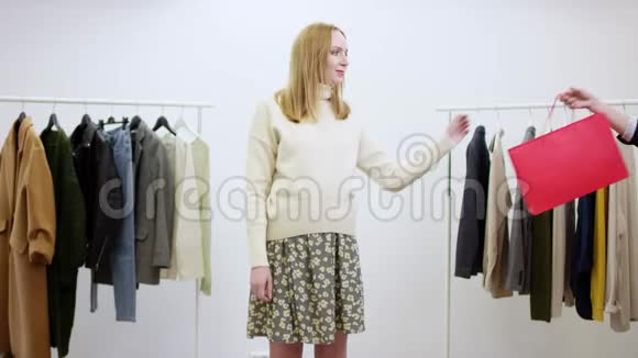 穿着毛衣和连衣裙的漂亮女人在一个服装室里向相机展示销售包视频的预览图