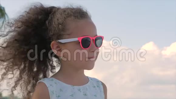 特写肖像一个漂亮的小女孩戴着粉红色的眼镜可爱的微笑着看着蓝天概念儿童视频的预览图