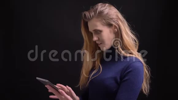 年轻的金发模特用平板电脑展示了它的绿色屏幕到相机以推荐黑色背景的应用程序视频的预览图