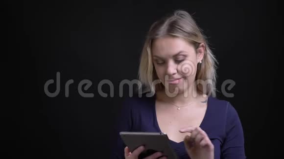 金发女商人打开平板电脑中的应用程序并在黑色背景下将其显示为相机的绿色屏幕视频的预览图