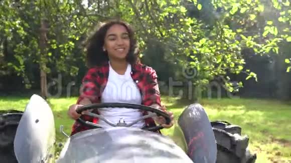 美国黑人混血少女驾驶灰色拖拉机穿过阳光明媚的苹果园视频的预览图