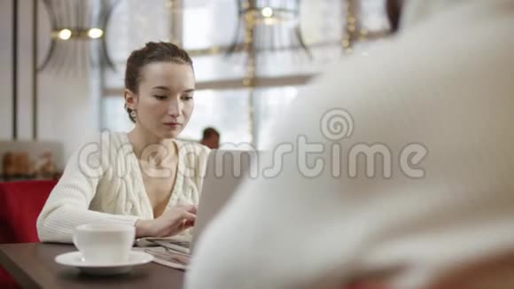 一位年轻的女士正在用笔记本电脑工作在咖啡馆里和她的朋友聊天视频的预览图