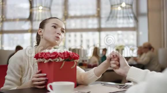年轻的女人握着丈夫的手盯着他的眼睛另一只手拿着一盒花在餐馆里视频的预览图