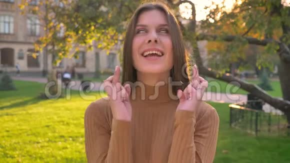 年轻的白种人黑发女孩在绿色公园的背景下幸福地交叉手指视频的预览图