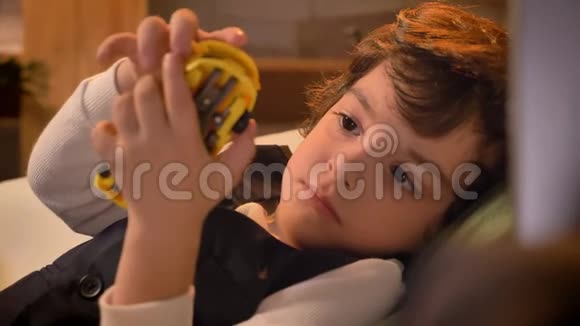 可爱的阿拉伯卷发男孩躺在沙发上在客厅玩玩具的特写肖像视频的预览图