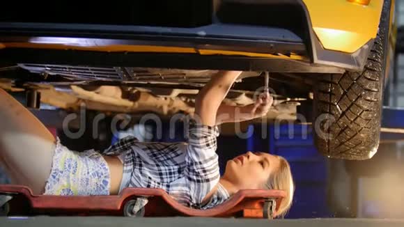 汽车服务机械师女孩穿着小短裤躺在车下修理它用扳手工作视频的预览图