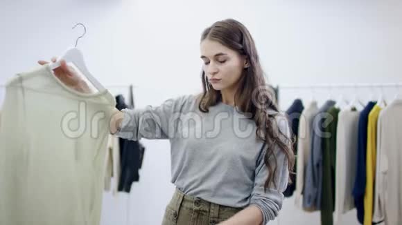 严肃的女人拿着毛衣件毛衣在一个服装室里检查它视频的预览图