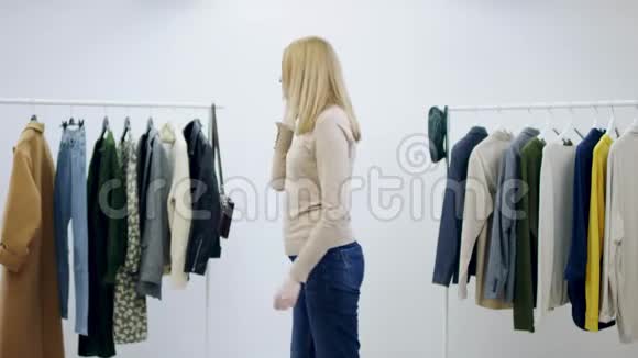 年轻貌美的女人在试衣间里看着衣服时正在谈论智能手机视频的预览图