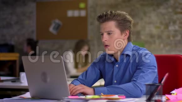 中年金发商人在办公室里拿着笔记本电脑和咳嗽的肖像视频的预览图