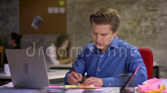 中年金发商人观看笔记本电脑并在办公室做笔记的肖像视频的预览图