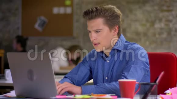 中年金发商人在办公室的笔记本电脑上打字的肖像靠在椅子上喝着咖啡视频的预览图