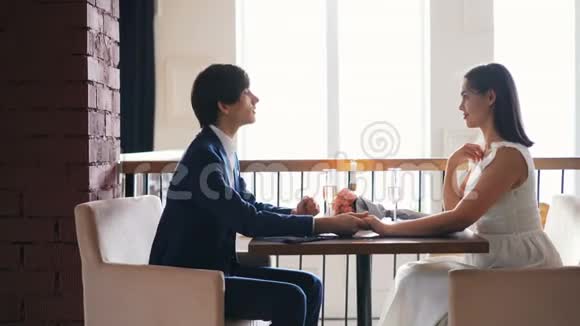 漂亮的年轻女子在餐馆里为求婚而兴奋而她的男朋友则在聊天然后戴上戒指视频的预览图