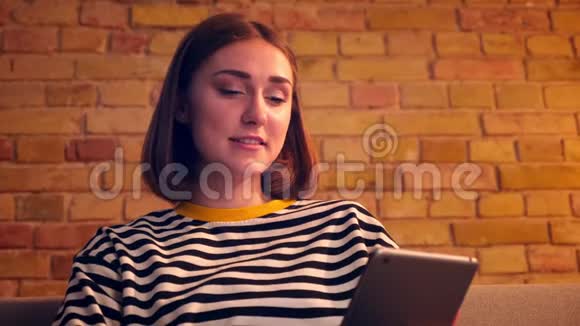 特写照片上年轻漂亮的女孩在平板电脑上打了个视频电话兴高采烈地坐在沙发上聊天视频的预览图