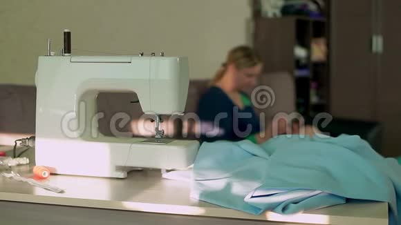 缝纫机回家在桌子上工作场所在背景中一位女裁缝正在研究一部智能手机视频的预览图