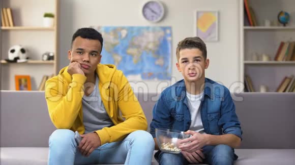 无聊的多种族男孩看电视吃零食慢的旧技术连接视频的预览图