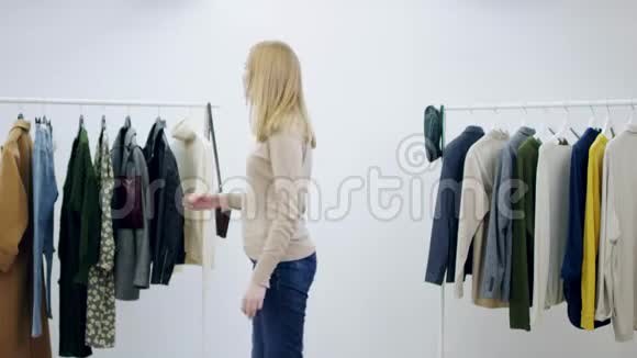 年轻的白种人女人正在一间满是衣服的房间里展示一件连衣裙视频的预览图