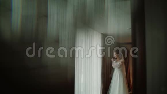 年轻漂亮的新娘站在窗边等着新郎望着窗外视频的预览图