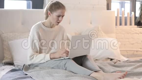 年轻女子在床上坐着面对笔记本电脑上的损失视频的预览图