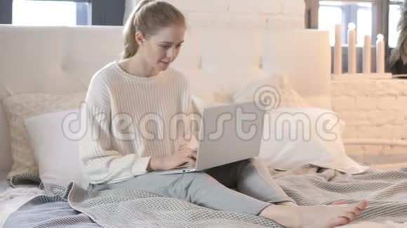 年轻女子坐在床上庆祝电脑成功视频的预览图