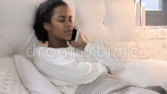 年轻的非洲女人在床上放松时打电话视频的预览图