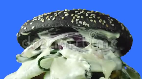 镜头自上而下的飞行是通过一个多汁的汉堡特写里面有一个黑色的面包绿色的受污染的白酱和一个视频的预览图