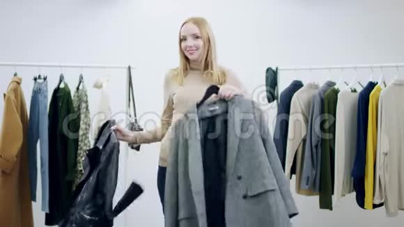有魅力的年轻女子在更衣室里展示一件外套和一件皮夹克视频的预览图