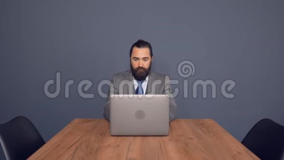 有胡子的商人坐在办公桌上用笔记本电脑工作视频的预览图