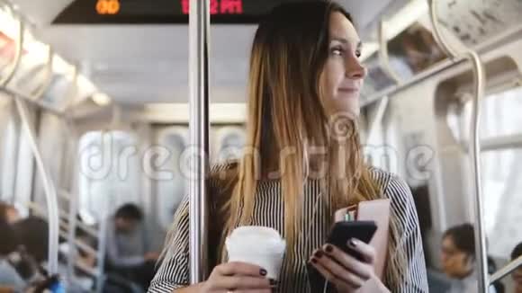 快乐轻松美丽的女性自由职业者坐在地铁列车上用购物软件微笑着看着智能手机视频的预览图
