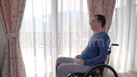 坐轮椅的沮丧青年在家窗户附近视频的预览图