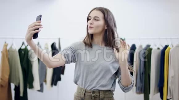 一位性格开朗的年轻女性在服装室的智能手机摄像头上拍照视频的预览图