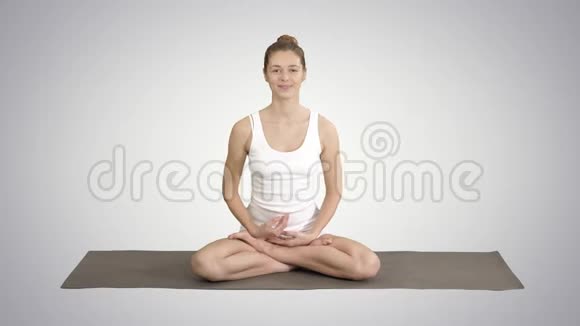 美丽的女人穿着白色的紧身衣坐在瑜伽垫上在渐变的背景上和相机交谈视频的预览图