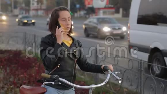 时尚有魅力的女孩坐在自行车上在城市和汽车的背景下打电话现代视频的预览图