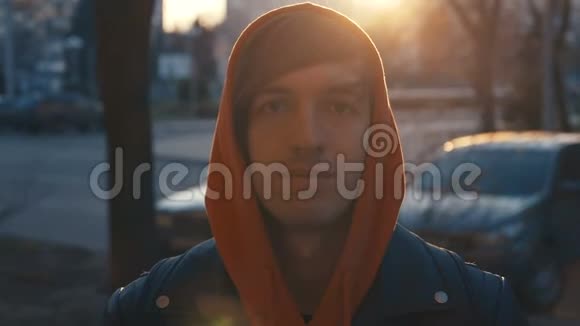 穿着帽衫的年轻人微笑着看着日落时的相机城市街头快乐帅哥的画像视频的预览图