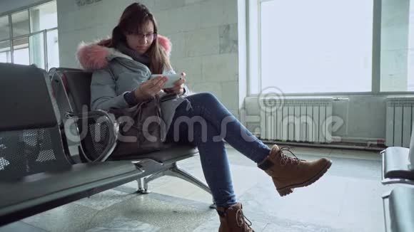 坐在火车站的年轻女人带着智能手机的肖像视频的预览图