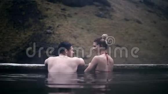 年轻的情侣一起在温泉里游泳在冰岛的山谷里男人和女人在水中放松视频的预览图
