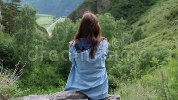 一位年轻的梦幻女子坐在群山的背景上头发飞扬慢动作视频的预览图