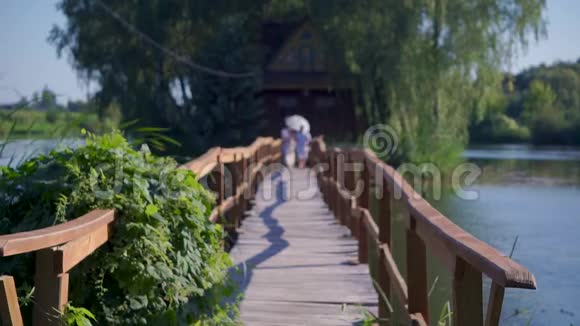恋爱中的男人和女人在夏日的白色雨伞下走在一座木桥上视频的预览图