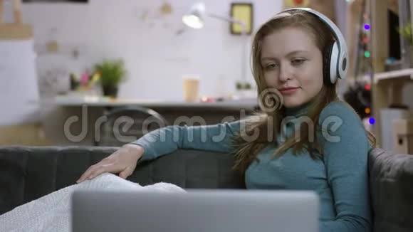 戴着耳机在沙发上看电影的年轻女子视频的预览图